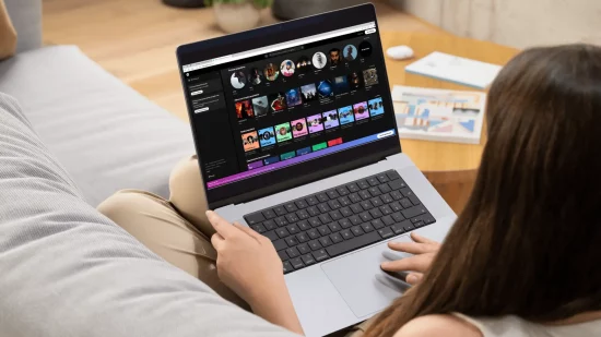 Une jeune femme dans son canapé écoutant Spotify depuis son PC portable